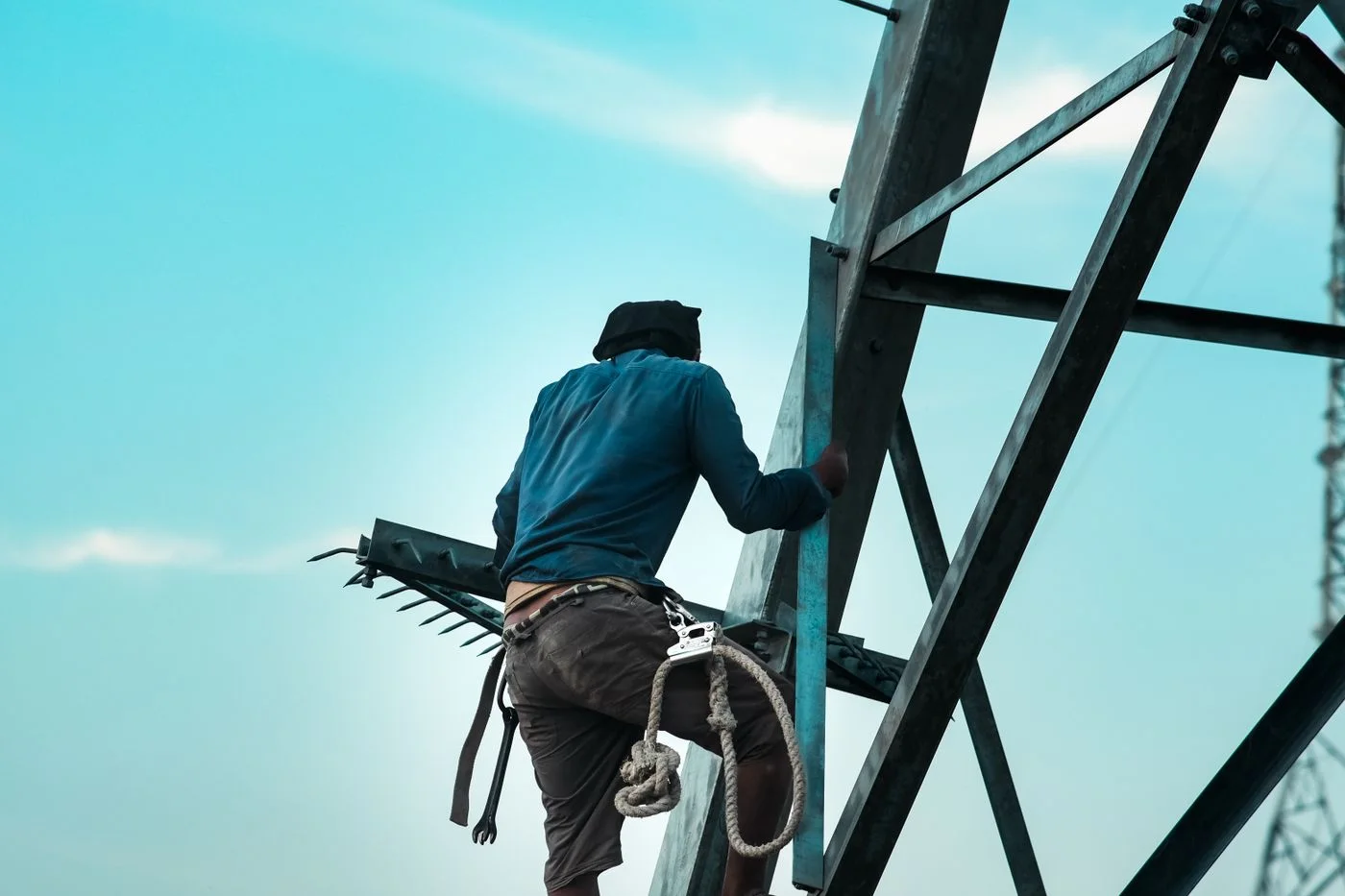 Professional climbing a steel structure with a safety lanyard attached at the waist